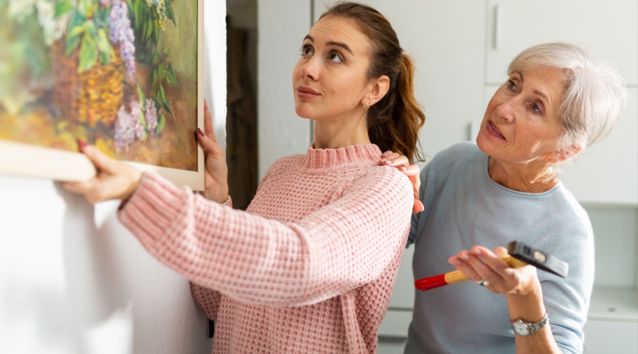 Daughter helping elder mother with hanging a painting