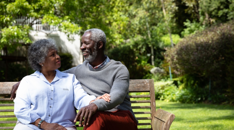 Elder couple sitting on bench smiling outside of home
